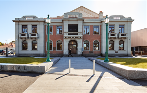 Photograph depicting the Williamstown Town Hall, an ornate red brick and cream render two story building, the Ada Cambridge forecourt featuring the green heritage street lights