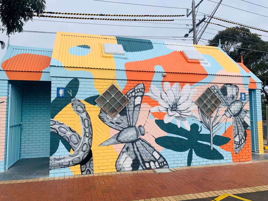 A colourful mural on a brick wall, featuring butterflies, a flower and a snake against a blue, orange and yellow background