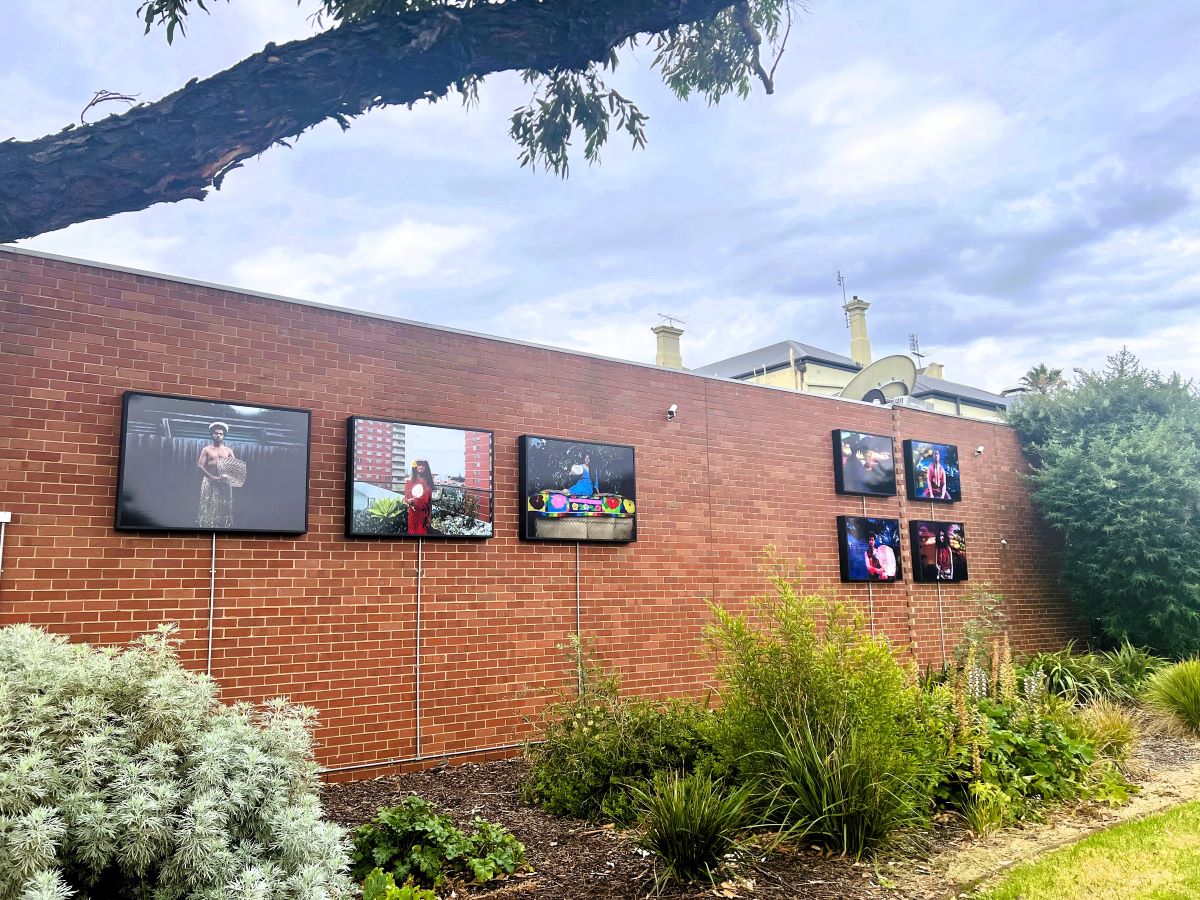 An exterior brick wall with seven lightboxes on it, displaying artwork.